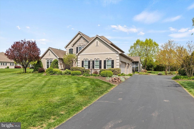 view of front of house with an attached garage, a front lawn, asphalt driveway, stucco siding, and stone siding