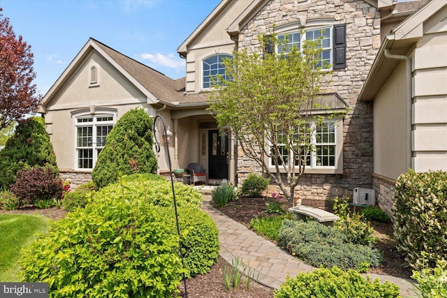 view of front of house featuring stone siding, stucco siding, and a shingled roof