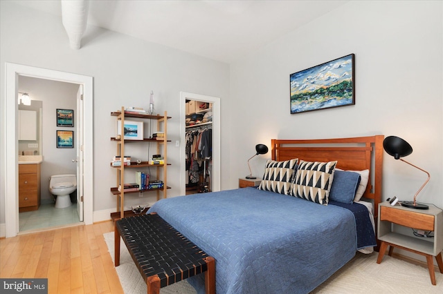 bedroom featuring a spacious closet, light wood-style floors, a closet, ensuite bathroom, and baseboards