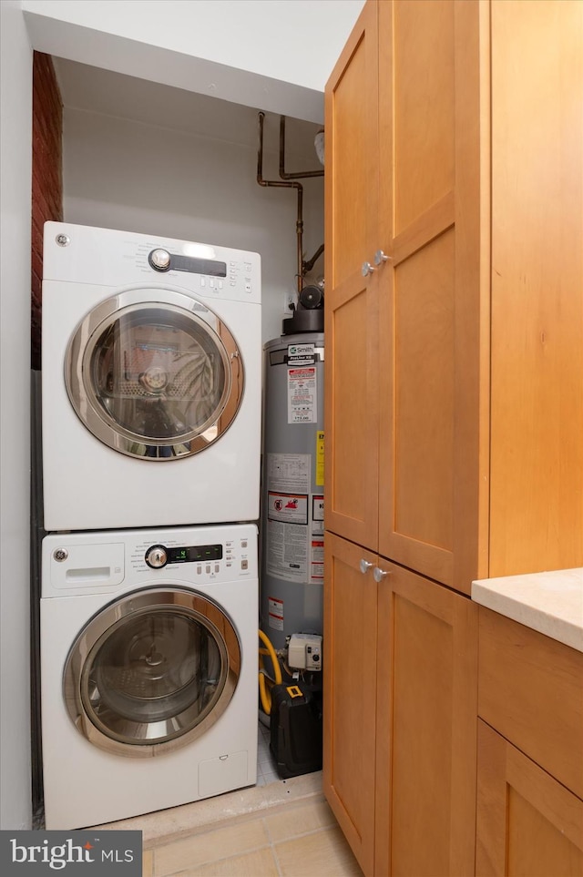 laundry area featuring stacked washer / drying machine, gas water heater, cabinet space, and light tile patterned floors