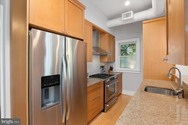 kitchen with appliances with stainless steel finishes, wall chimney exhaust hood, a sink, tasteful backsplash, and light stone countertops