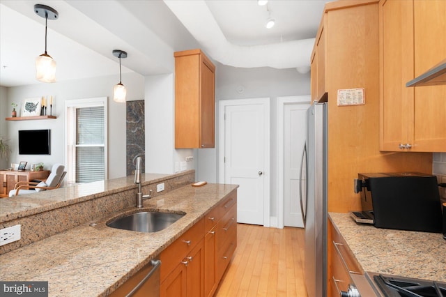 kitchen featuring a sink, appliances with stainless steel finishes, light wood-style floors, light stone counters, and decorative light fixtures