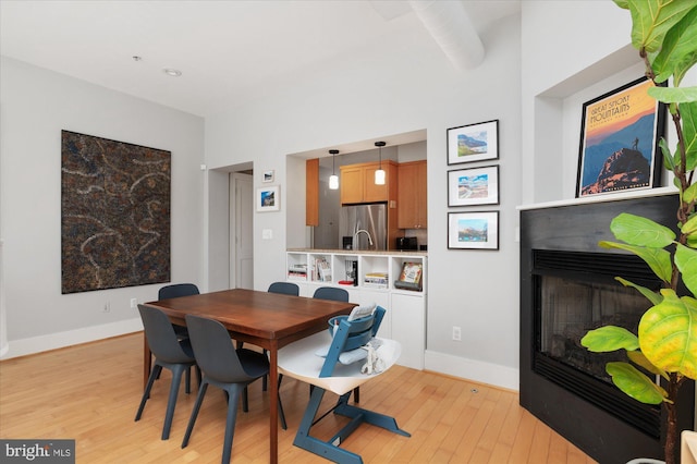 dining area featuring light wood-type flooring, baseboards, and a glass covered fireplace