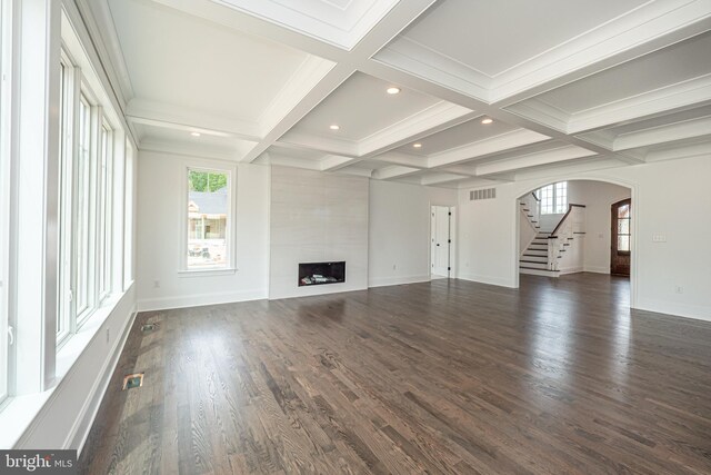 unfurnished living room with arched walkways, plenty of natural light, beamed ceiling, stairs, and baseboards