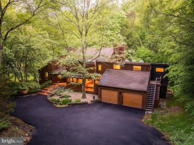 view of front facade with a view of trees, asphalt driveway, stairs, and an attached garage