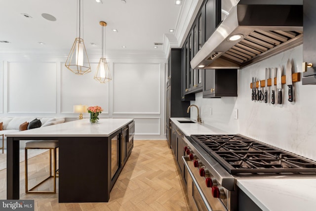 kitchen featuring wall chimney range hood, a sink, cooktop, dark cabinetry, and decorative light fixtures