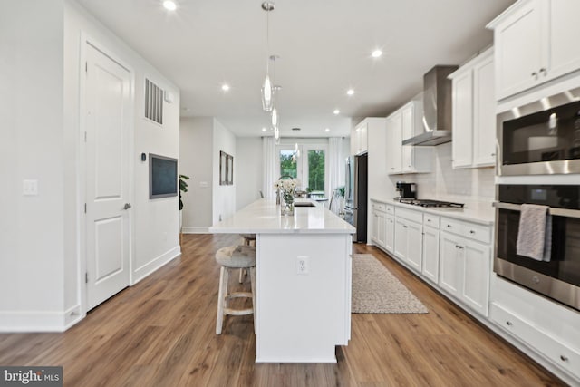 42089 Shining Star Sq, Brambleton, VA 20148 - kitchen with stainless steel appliances, an island with sink, wall chimney exhaust hood, white cabinetry, and wood finished floors