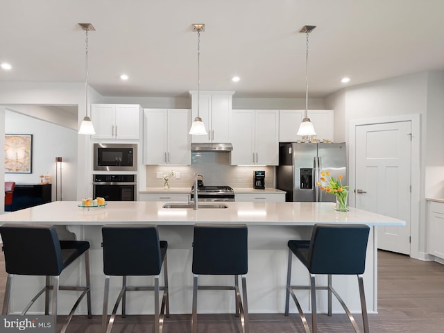 kitchen with stainless steel appliances, under cabinet range hood, a sink, decorative backsplash, and light countertops