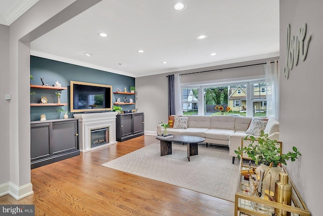 living room featuring crown molding, recessed lighting, light wood finished floors, a glass covered fireplace, and baseboards