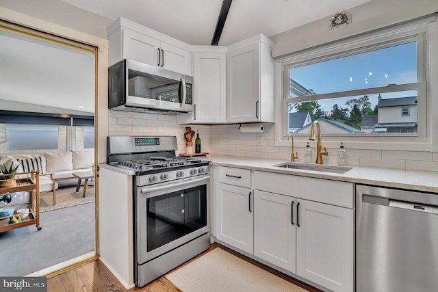 kitchen with stainless steel appliances, a sink, light countertops, and white cabinetry