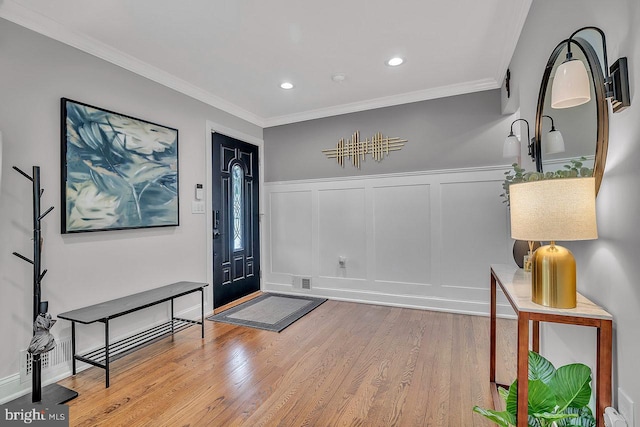 entryway with a decorative wall, crown molding, wood finished floors, wainscoting, and recessed lighting