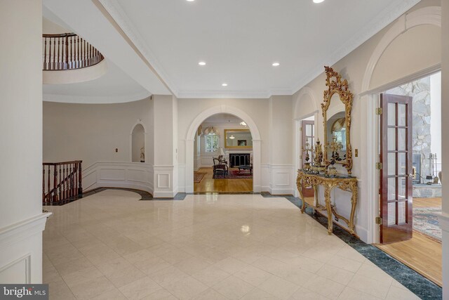 hall featuring a decorative wall, ornamental molding, recessed lighting, arched walkways, and a wainscoted wall