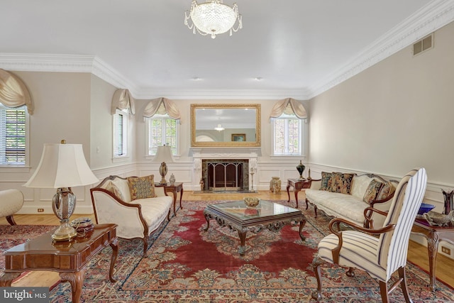 living room with a decorative wall, ornamental molding, a chandelier, a wainscoted wall, and a high end fireplace