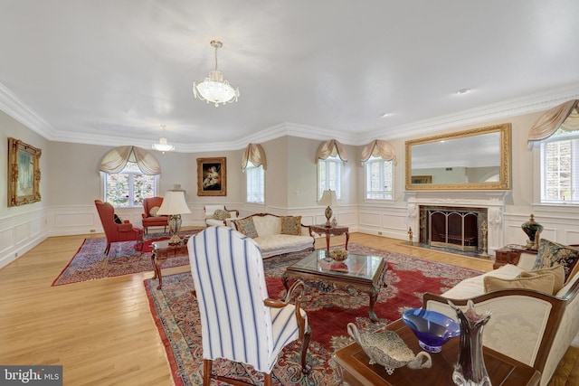 living area featuring healthy amount of natural light, a decorative wall, light wood finished floors, a chandelier, and crown molding