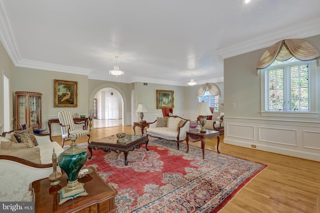 living area featuring arched walkways, ornamental molding, light wood finished floors, a wainscoted wall, and a decorative wall