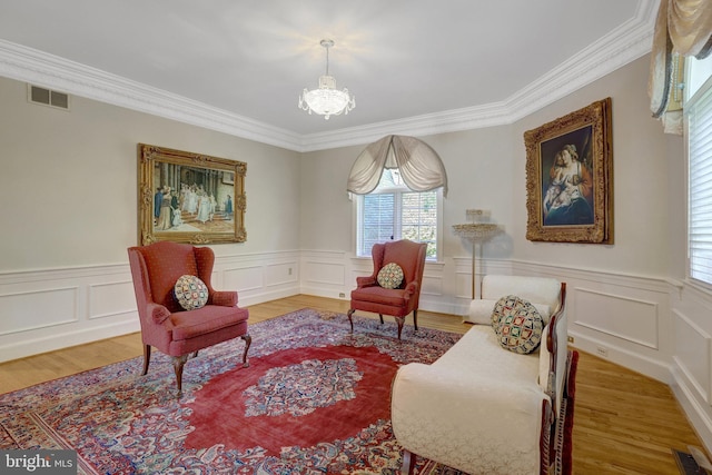 sitting room featuring a chandelier, crown molding, wainscoting, wood finished floors, and a decorative wall