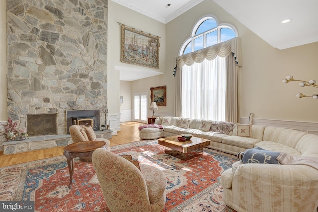 living area with wood finished floors, a stone fireplace, a wainscoted wall, a towering ceiling, and ornamental molding