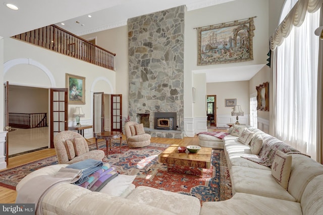 living area featuring plenty of natural light, a towering ceiling, wood finished floors, wainscoting, and a fireplace