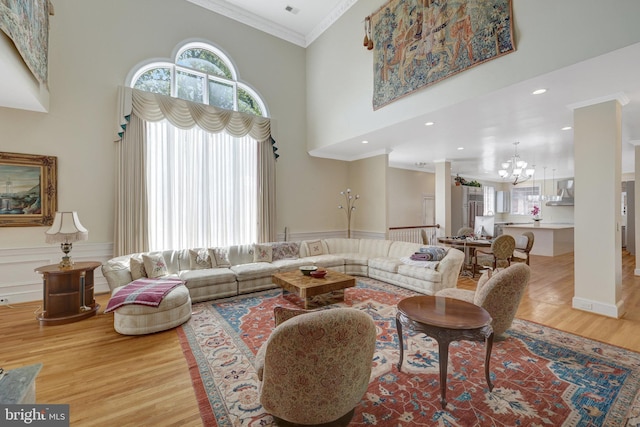 living area featuring a chandelier, crown molding, wood finished floors, a towering ceiling, and wainscoting