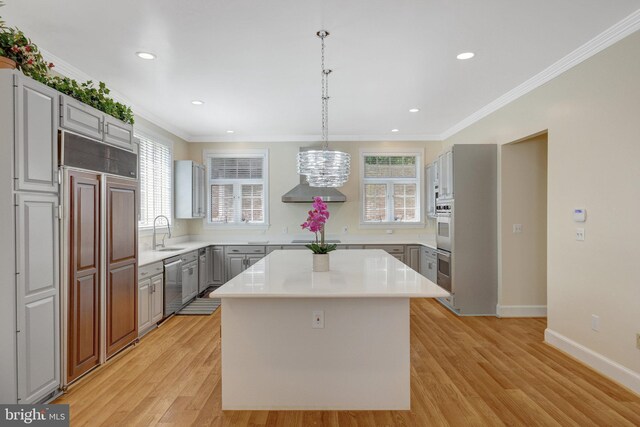 kitchen featuring stainless steel appliances, light wood-style flooring, a sink, light countertops, and crown molding