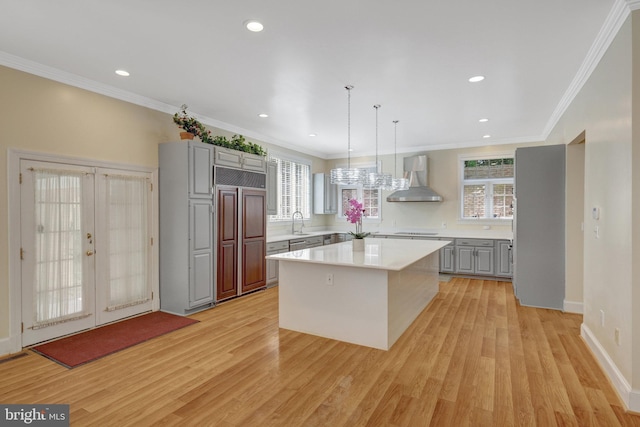 kitchen with wall chimney exhaust hood, gray cabinets, paneled refrigerator, light wood-style flooring, and light countertops