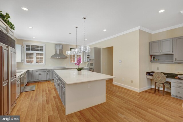 kitchen with gray cabinets, wall chimney range hood, ornamental molding, light wood-type flooring, and a kitchen island
