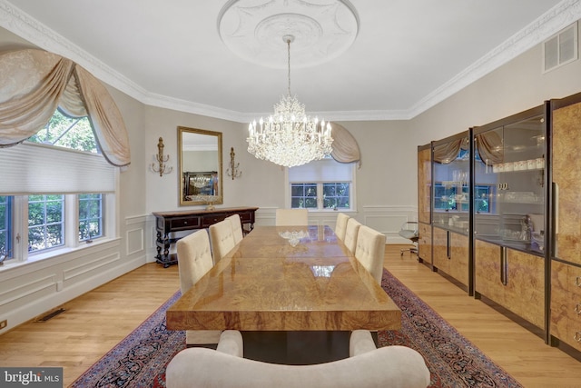 dining space with a chandelier, light wood-style floors, a decorative wall, ornamental molding, and wainscoting