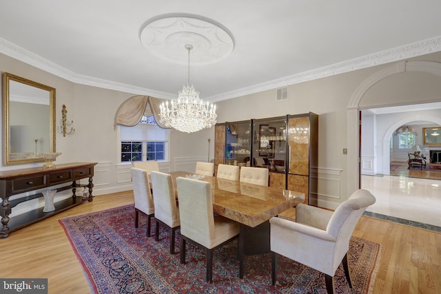 dining space featuring a chandelier, a decorative wall, wood finished floors, crown molding, and arched walkways