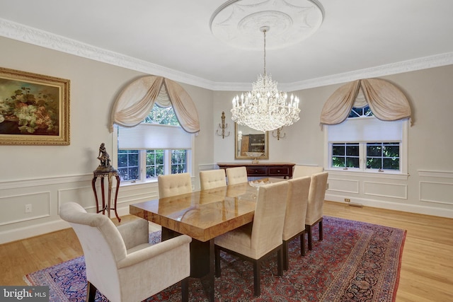 dining room featuring a chandelier, light wood-style floors, a decorative wall, wainscoting, and ornamental molding