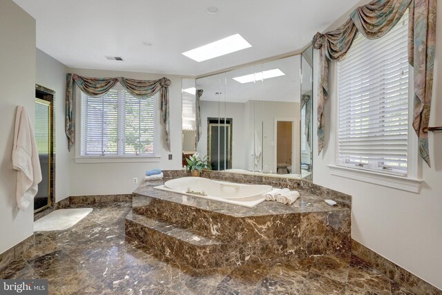bathroom with marble tiled flooring, a skylight, a bath, and a shower stall