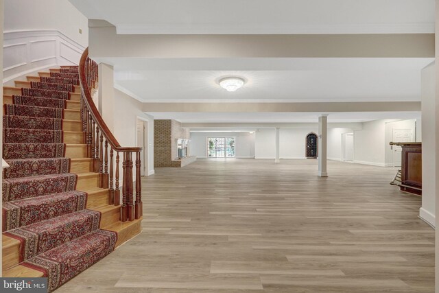entryway with stairs, light wood-style floors, ornamental molding, a brick fireplace, and baseboards