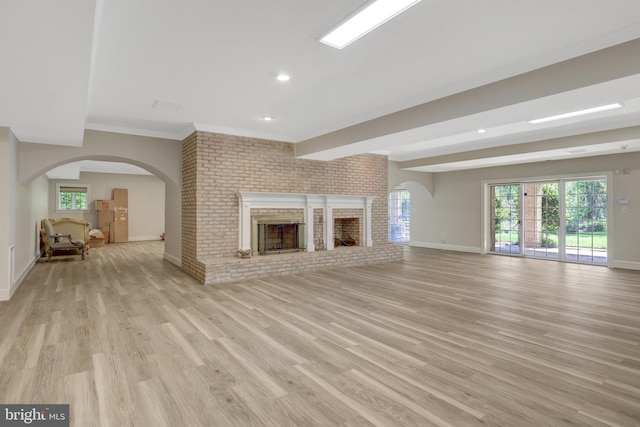 unfurnished living room with baseboards, light wood-style flooring, plenty of natural light, arched walkways, and brick wall