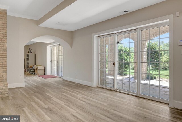 unfurnished living room featuring arched walkways, wood finished floors, baseboards, and crown molding