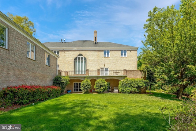 rear view of house with a lawn, brick siding, and a balcony