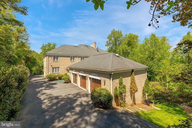 view of property exterior with brick siding, an attached garage, and asphalt driveway