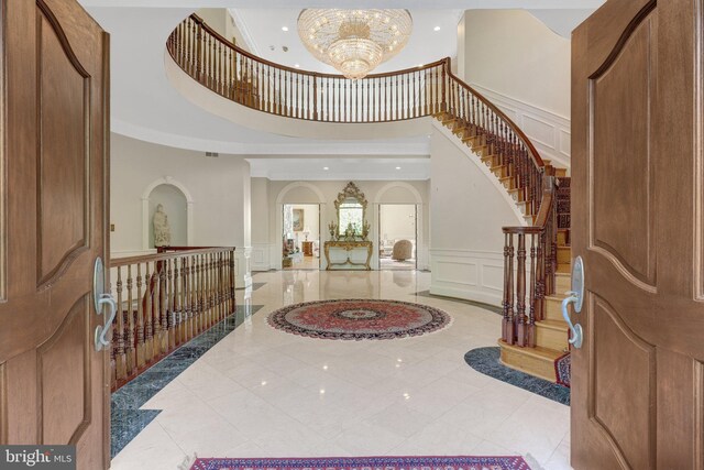 entrance foyer with a decorative wall, a towering ceiling, a chandelier, arched walkways, and stairway