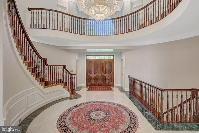 entryway with a towering ceiling, inlaid floor details, a chandelier, stairs, and baseboards