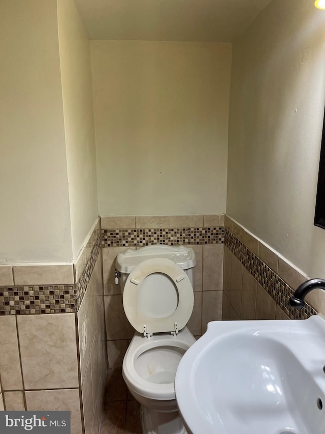 437 52nd St, Baltimore, MD 21224 - half bath with tile walls, a sink, wainscoting, and toilet