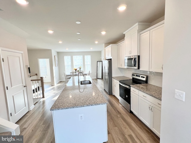 kitchen featuring stainless steel appliances, a sink, a kitchen island with sink, white cabinets, and light wood-type flooring