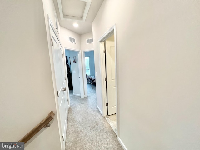 corridor with light colored carpet, attic access, and baseboards