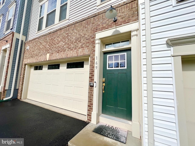 view of exterior entry featuring brick siding, an attached garage, and asphalt driveway