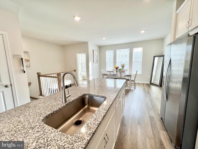 kitchen featuring stainless steel fridge, a sink, light wood-style floors, white cabinets, and light stone counters