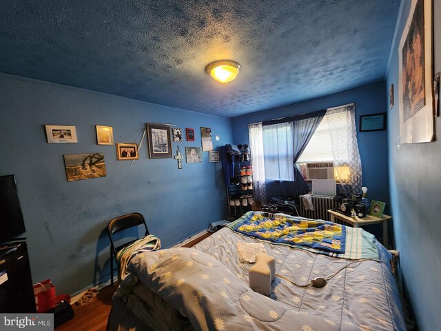 1351 Cambria St, Baltimore, MD 21225 - bedroom featuring a textured ceiling, radiator, wood finished floors, cooling unit, and baseboards