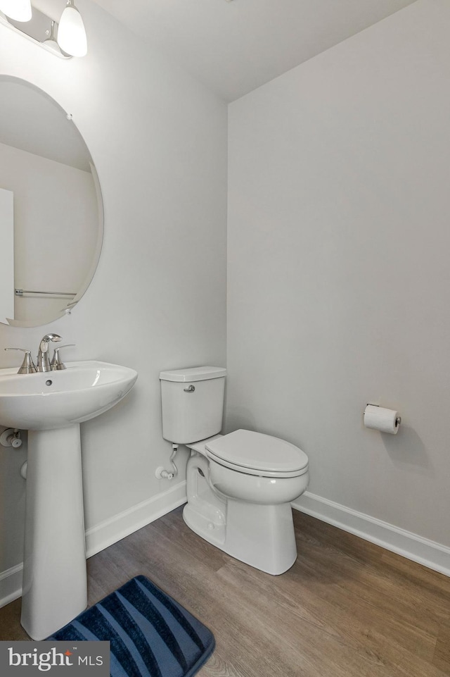half bathroom featuring wood finished floors, toilet, and baseboards