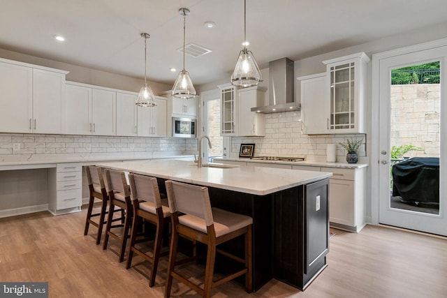 kitchen with wall chimney range hood, a sink, stainless steel appliances, light wood-style floors, and recessed lighting