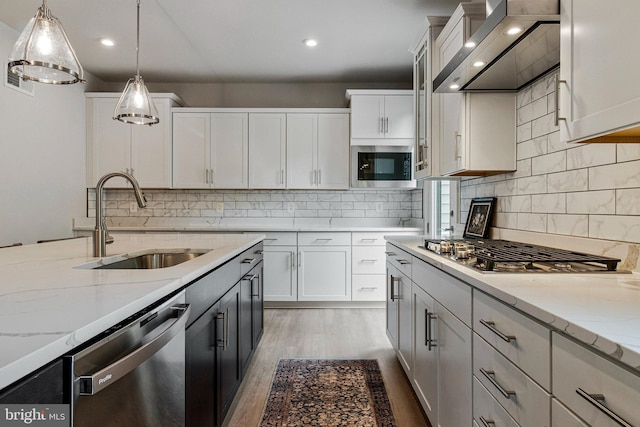 kitchen with wall chimney exhaust hood, stainless steel appliances, a sink, light wood-style floors, and hanging light fixtures