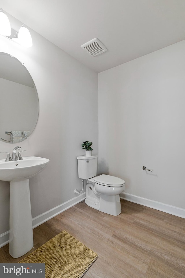 half bathroom with wood finished floors, toilet, baseboards, and a sink