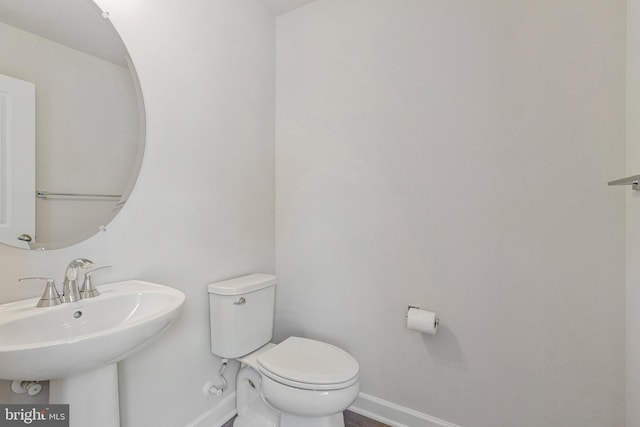 half bathroom with baseboards, a sink, and toilet