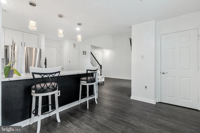 kitchen featuring freestanding refrigerator, a kitchen bar, dark wood-style flooring, baseboards, and decorative light fixtures