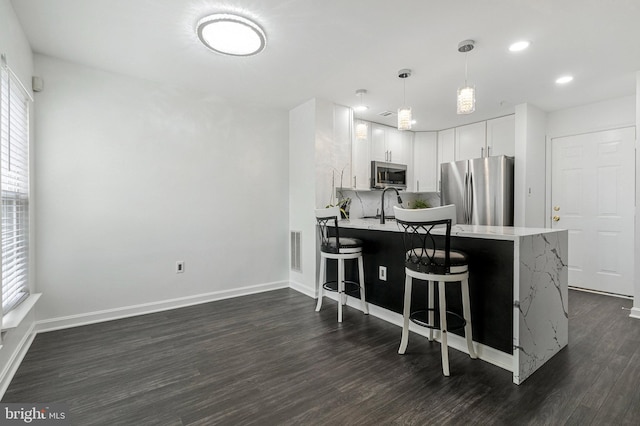 kitchen featuring stainless steel appliances, light countertops, a peninsula, dark wood-style floors, and a breakfast bar area